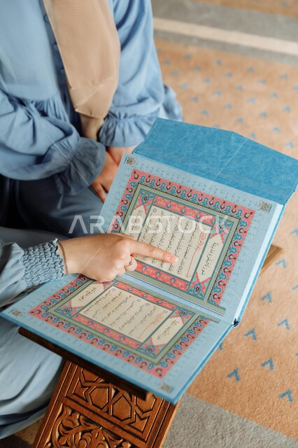تربية الأبناء على المعايير الإسلامية منذ الصغر، صورة مقربة من الأعلى لأم عربية خليجية سعودية تقوم بتعليم ابنتها قواعد التجويد الصحيحة، تلاوة القرآن الكريم وحفظ كتاب الله، تفسير الآيات والسور وفهم المعاني والعبر، قراءة المصحف الشريف بتمعن والتقرب لله تعالى