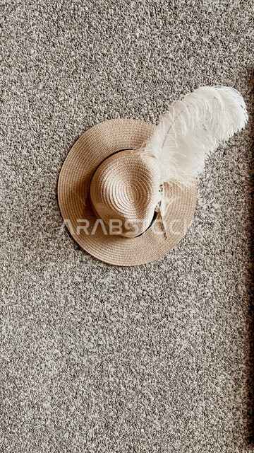 قبعة رأس نسائية منسوجة بالقش ذات لون بيج جميل مع ريشة بيضاء رائعة موضوعة على أرضية سجادة