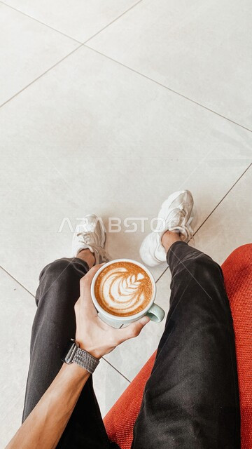 صورة من أعلى لفنجان من القهوة الكابتشينو الساخنة بيد شاب في مقهى ، شرب القهوة في محل القهوة 