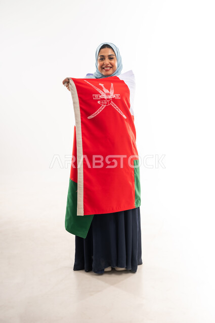 Participating in national holidays and occasions, celebrating Oman National Day November 18, commemorating the independence of the state 1650 AD, portrait of a smiling young Omani Gulf Arab woman wearing an abaya carrying the flag of the Sultanate of Oman on her back, pride and honor in Omani symbols, full body image, white background