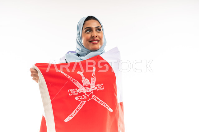 مفهوم حب الوطن والانتماء اليه، المشاركة بالاعياد والمناسبات الوطنية، اليوم الوطني العماني 18نوفمبر, احياء ذكرى استقلال الدولة1650م، بورتريه مقرب لشابة عربية خليجية عمانية ترتدي العباءة تحمل علم سلطنة عمان على ظهرها، الاعتزاز والفخر بالرموز العمانية، خلفية بيضاء