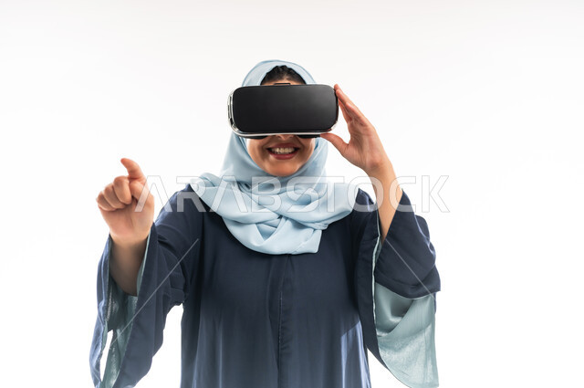الاندماج ومحاكاة العالم الخيالي، محاولة النقر على شيء ما, المتعة والتسلية بالمشاهدة عبر نظارة الواقع الافتراضي، بورتريه مقرب لإمرأة عربية خليجية عمانية ترتدي العباءة تضع نظارات ثلاثية الابعاد, شابة سعودية ترفع اصبع السبابة والاشارة الى مكان معين، خلفية بيضاء