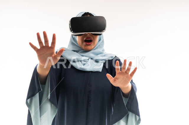 Using virtual reality technology, a young Saudi woman raises her hands to try to touch something with immersion gestures, simulating the imaginary world through VR glasses, a close-up portrait of an Arab Gulf Omani woman wearing an abaya, putting on 3D glasses and moving and interacting with them, white background