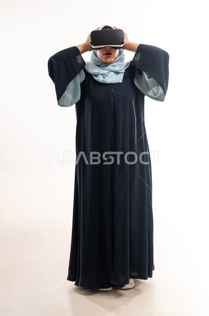 الاندماج ومحاكاة العالم الخيالي عبر نظارة الواقع الافتراضي،  بورتريه لإمرأة عربية خليجية عمانية ترتدي العباءة تنظر من خلال نظارات ثلاثية الأبعاد، شابة سعودية تضع يدها على رأسها بتعابير الاندهاش والتفاجؤ، التطور التقني والتكنولوجي, الطول الكامل للجسم، خلفيه يضاء