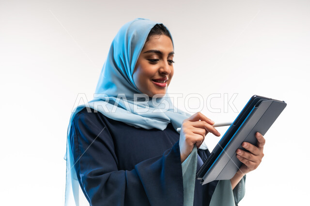 Browsing social media sites and media, integrating technology and modern technology into daily and practical life, close-up portrait of an Arab Gulf Omani woman wearing an abaya writing on a tablet, concept of remote project completion, young Saudi woman holding a tablet, white background