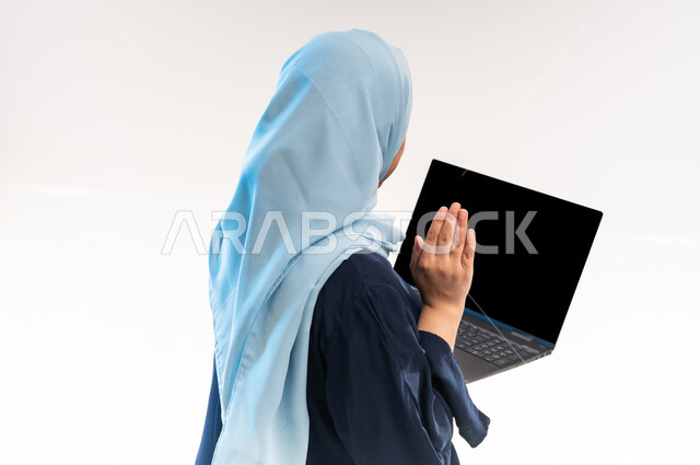 Greeting, welcoming and saying hello, integrating modern technology into daily life, close-up portrait from back of an Arab Gulf Omani woman wearing an abaya making a video call, young Saudi woman using laptop, communicating with family and friends, white background