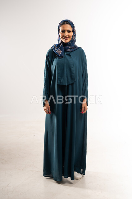 التقاط صور شخصية للوثائق الرسمية، سيدة سعودية تنظر إلى الكاميرا بتعابير السعادة، الاهتمام بالمظهر الخارجي، مفهوم الأناقة والأنوثة, بورتريه لامرأة عربيه عمانية محجبة ترتدي العباءه تقف باستقامة واعتدال بايماءات الثقة بالنفس, الطول الكامل للجسم, خلفية بيضاء