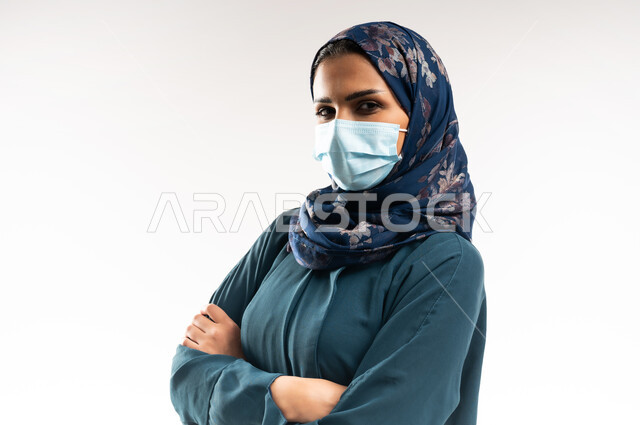 الاهتمام بالمظهر الخارجي، مفهوم الأناقة والأنوثة, بورتريه مقرب لامرأة عربيه عمانية محجبة ترتدي العباءه تقف بأيدي متقاطعة بايماءات الثقة بالنفس, الحفاظ على السلامة من كوفيد 19، سيدة سعودية تضع الكمامة وتنظر إلى الكاميرا، خلفية بيضاء