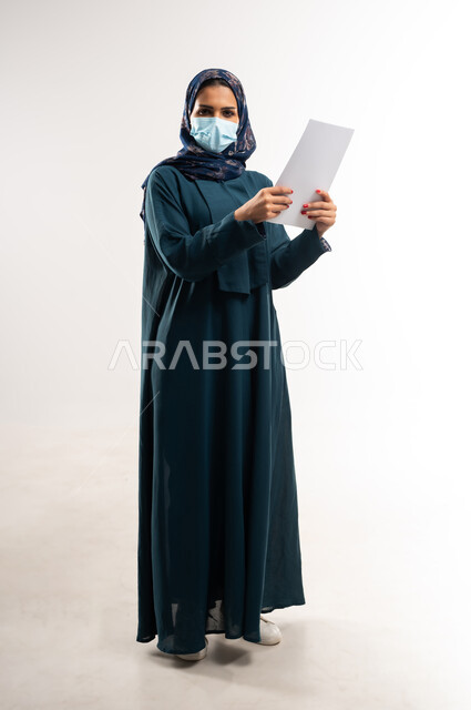 لوحات توعوية لتجنب إنتشار العدوى، اتباع الاجراءات الاحترازية للوقاية من فايروس كورونا، بورتريه لإمرأة عربية خلجية عمانية محجبة ترتدي العباءة وتضع الكمامة، سيدة سعودية تمسك أوراق بيضاء فارغة, الحفاظ على السلامة من كوفيد 19، الجسم بالطول الكامل، خلفية بيضاء