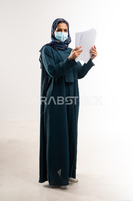 لوحات توعوية لتجنب إنتشار العدوى، اتباع الاجراءات الاحترازية للوقاية من فايروس كورونا، بورتريه لإمرأة عربية خلجية عمانية محجبة ترتدي العباءة وتضع الكمامة، سيدة سعودية تمسك أوراق بيضاء فارغة, الحفاظ على السلامة من كوفيد 19، الجسم بالطول الكامل، خلفية بيضاء