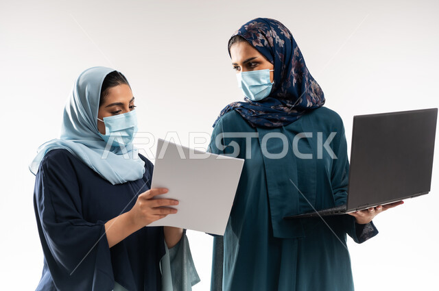 تبادل الخبرات  الناجحة, التفاهم بين سيدات الأعمال السعودية في,  بورتريه مقرب لامرأتين عربيتين خليجيتين عمانيتين ترتديان العباءة والكمامة تقومان بالعمل على اللابتوب، استخدام التكنولوجيا الحديثة في متابعه سير العمل، الاحترافية والتفاني في الانجاز, خلفية بيضاء