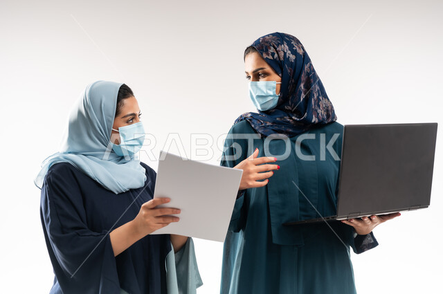 الاحترافية والتفاني في الانجاز, تبادل الخبرات  الناجحة, التفاهم بين سيدات الأعمال السعودية في,  بورتريه مقرب لامرأتين عربيتين خليجيتين عمانيتين ترتديان العباءة والكمامة تقومان بالعمل على اللابتوب، استخدام التكنولوجيا الحديثة في متابعه سير العمل، خلفية بيضاء