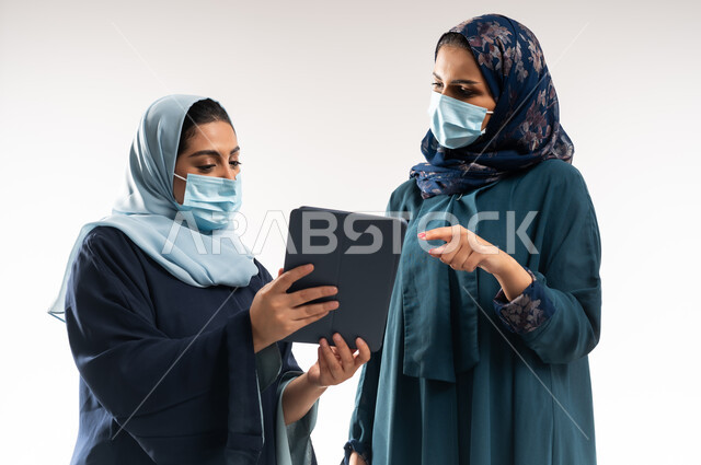 Business and corporate development, use of modern technology to monitor workflow, cooperation between Saudi businesswomen, close-up portrait of two Gulf Arab Omani women wearing abaya working on tablet, focus and perfect work, white background