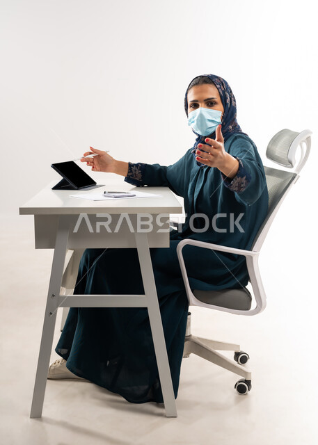 اعطاء الاوامر والتعليمات بعصبية، الاشارة الى احد ما بايماءات الغصب والتوبيخ، تعابير الضغط العصبي والتوتر، بورتريه من الجانب لإمرأة عربية خليجية عمانية ترتدي العباءة تعمل على جهاز اللابتوب، سيدة سعودية تضع الكمامة للوقائية من فايروس كورونا, خلفية بيضاء