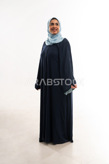 النظرة المستقبلية والتفكير لتحقيق النجاح, الاهتمام بالمظهر الخارجي، مفهوم الأناقة والأنوثة, بورتريه لامرأة عربيه عمانية محجبة ترتدي العباءه تنظر الى شيء ما, سيدة سعودية تقف باستقامة واعتدال بايماءات الثقة بالنفس, الطول الكامل للجسم, خلفية بيضاء