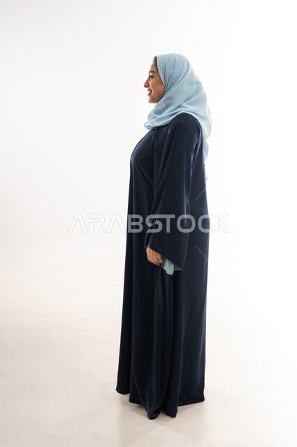 Concern for appearance, concept of elegance and femininity, side portrait of a veiled Omani Arab woman wearing an abaya looking at something, Saudi woman standing straight and looking to the left, future outlook and thinking to achieve success, full body length, white background
