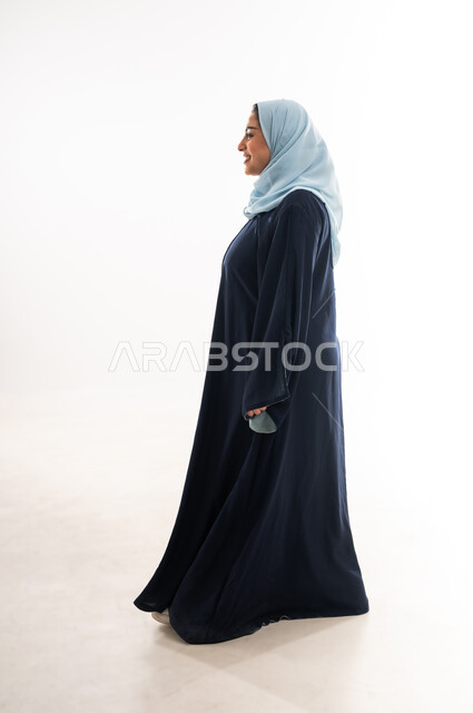 ايماءات الذهاب إلى مكان معين، بورتريه من الجانب لإمرأة عربية خليجية عمانية محجبة ترتدي العباءة تنظر إلى شيء ما، التقدم إلى الأمام بخطوات ثابتة، سيدة سعودية تمشي بتعابير السعادة، الاهتمام بالمظهر الخارجي، مفهوم الأناقة والأنوثة, الطول الكامل للجسم، خلفية بيضاء
