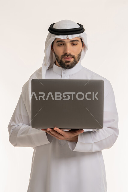 مفهوم العمل عن بعد, بورتريه لشاب عربي خليجي سعودي يرتدي الثوب التقليدي والغترة يستخدم الحاسب المحمول, التواصل والدردشة مع الأصدقاء والأهل عبر السوشال ميديا, دمج العمل مع التقنية والتكنولوجيا الحديثة والمتطورة, ادارة المهام عبر الأونلاين, خلفية بيضاء