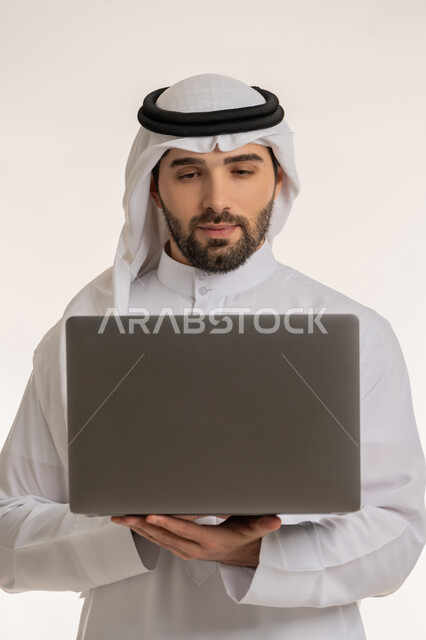 ادارة المهام عبر الأونلاين, مفهوم العمل عن بعد, بورتريه مقرب لشاب عربي خليجي سعودي يرتدي الثوب التقليدي والغترة يستخدم الحاسب المحمول, التواصل والدردشة مع الأصدقاء والأهل عبر السوشال ميديا, دمج العمل مع التقنية والتكنولوجيا الحديثة والمتطورة, خلفية بيضاء