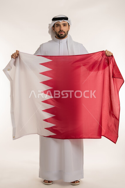 إحياء ذكرى تأسيس الدولة، الاحتفال باليوم الوطني القطري 18 ديسمبر، بورتريه لرجل عربي خليجي قطري يحمل علم قطر بايماءات الفخروالاعتزاز، رموز وثقافات وطنية, حب الوطن والانتماء إليه، الطول الكامل للجسم، خلفية بيضاء