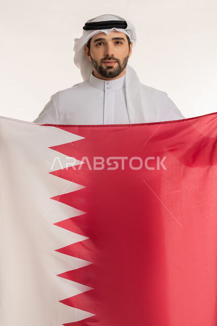 Patriotism and belonging to the homeland, celebrating Qatar National Day December 18, commemorating the founding of the state, close-up portrait of a Qatari Gulf Arab man holding the Qatari flag with gestures of pride and honor, national symbols and cultures, white background