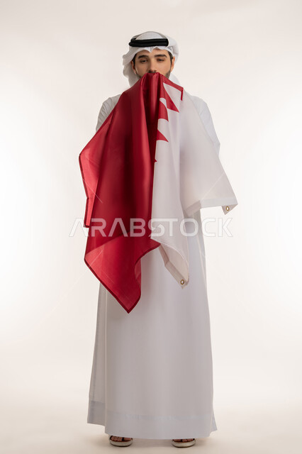 إحياء ذكرى تأسيس الدولة، الاحتفال باليوم الوطني القطري 18 ديسمبر، بورتريه لرجل عربي خليجي قطري يحمل علم قطر ويقوم بتقبيله بايماءات الفخروالاعتزاز، رموز وثقافات وطنية, حب الوطن والانتماء إليه، الطول الكامل للجسم، خلفية بيضاء