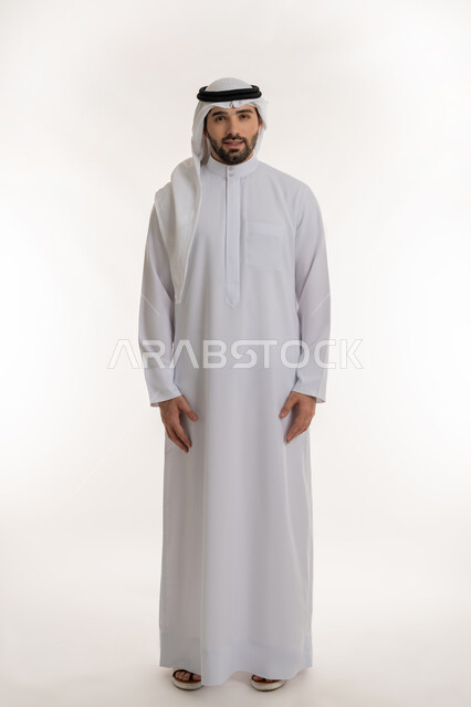 التقاط الصور الشخصية للوثائق الرسمية، بورتريه لشاب عربي خليجي سعودي يرتدي الثوب التقليدي والغترة ينظر الى الكاميرا بتعابير البشاشة، الأناقة والاهتمام بالمظهر الخارجي، الوقوف باستعداد واستقامة، مفهوم الرجولة والثقة بالنفس، الطول الكامل للجسم، خلفية بيضاء