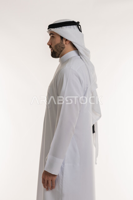 الاهتمام بالمظهر الخارجي, مفهوم الأناقة والرجولة, النظر الى مكان ما بايماءات الثقة بالنفس، بورتريه من الجانب لرجل عربي خليجي سعودي يرتدي الثوب التقليدي والغترة يقف باستقامة واعتدال, خلفية بيضاء