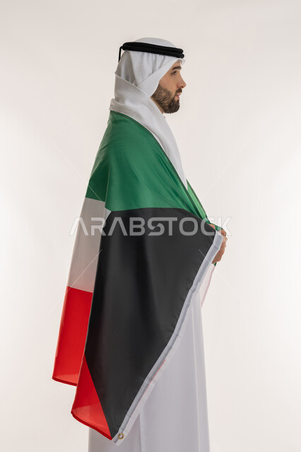 استذكار اليوم الوطني الكويتي في 25 فبراير, اظهار مشاعر الفخر بالانتماء للوطن, مناسبات وأعياد وطنية, بورتريه من الجانب لشاب عربي خليجي كويتي يرتدي الثوب التقليدي والغترة يضع على ظهره علم دولة الكويت باعتزاز, خلفية بيضاء