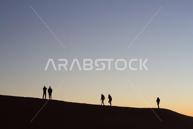 أماكن المغامرات والرحلات السياحية الممتعة, البيئة الصحراوية في المملكة العربية السعودية, التشكيلات والتكوينات الرملية في الصحراء, صورة ظليلة لمجموعة من الأشخاص يسيرون على الرمال في وقت غروب الشمس