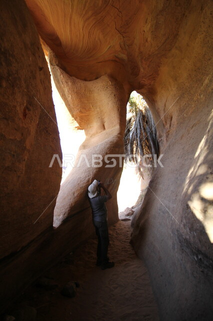 جذب و استقطاب الزائرين من شتى انحاء العالم, معالم و أماكن سياحية مشهورة في المملكة العربية السعودية, صورة من الخلف لسائح يقوم بالتقاط الصور التذكارية للتشكيلات و التكوينات الصخرية في وادي الديسة في منطقة تبوك في وقت النهار