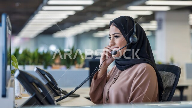 مهن ووظائف نسائية, متابعة وتطوير الأعمال، الإجابة على استفسارات العملاء, موظفة عربية خليجية سعودية مبتسمة محجبة تضع سماعات الرأس (الهيدفون) تجري مكالمة فيديو، العمل في المجال المكتبي, عقد اجتماع عمل عبر الانترنت