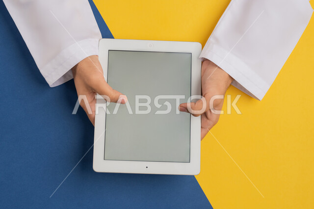 لعب الالعاب الالكترونية، متابعة الدروس التعليمية، بورتريه علوي عامودي لرجل عربي خليجي إماراتي يقوم بإنجاز المهام المطلوبة عن بعد، شاب سعودي يستخدام جهاز التابليت، التعليم عن بعد بواسطة الانترنت، الاستمتاع بمشاهدة الافلام ، عرض شاشة رمادية فارغة، خلفية ملونة