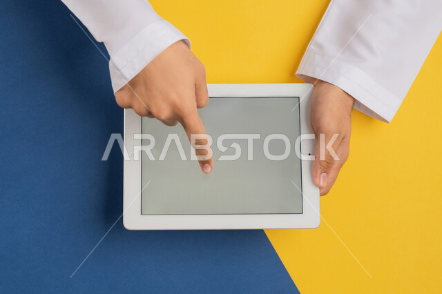 التعليم عن بعد بواسطة الانترنت، الاستمتاع بمشاهدة الافلام، عرض شاشة رمادية فارغة، لعب الالعاب الالكترونية، متابعة الدروس التعليمية، بورتريه علوي عامودي لرجل عربي خليجي إماراتي يقوم بإنجاز المهام المطلوبة عن بعد، شاب سعودي يستخدام جهاز التابليت، خلفية ملونة