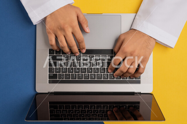 إنجاز المهام المطلوبة عن بعد، بورتريه علوي عامودي ليدين رجل عربي خليجي إماراتي يعمل على الحاسب المحمول، شاب سعودي يقوم بعرض شاشة سوداء فارغة على اللابتوب، دمج العمل مع التقنية والتكنولوجيا الحديثة، مفهوم ادارة الاعمال وتحقيق الأهداف أونلاين، خلفية ملونة