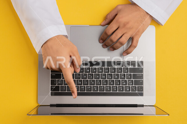 إنجاز المهام المطلوبة عن بعد، مفهوم ادارة الاعمال وتحقيق الأهداف، دمج التكنولوجيا الحديثة في الحياة العملية، بورتريه علوي عامودي لايدي رجل عربي خليجي اماراتي يستخدم الحاسوب المحمول، شاب سعودي يشير باصبعه السبابة على شاشة اللابتوب، خلفية صفراء