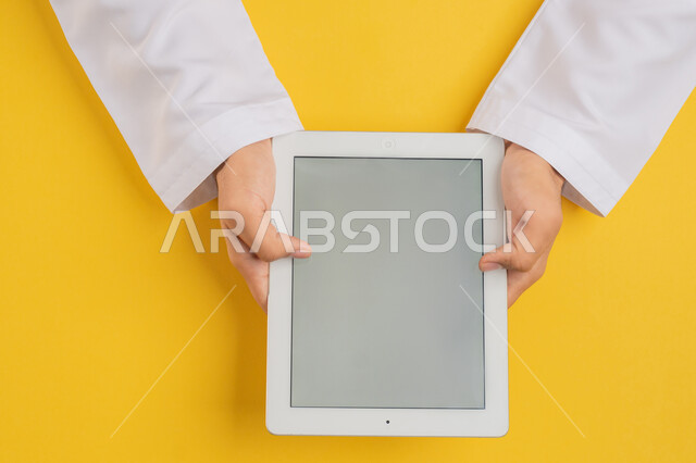 استخدام التكنولوجيا والاجهزة الحديثة، بورتريه ليد رجل عربي خليجي اماراتي يحمل بيديه جهاز التابلت، شاب سعودي يستخدم تقنية الايباد، الاستمتاع بمشاهدة الافلام والمسلسلات، عرض شاشة رمادية فارغة، متابعة الدروس التعليمية، خلفية صفراء