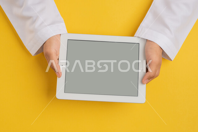 استخدام التكنولوجيا والاجهزة الحديثة، بورتريه ليد رجل عربي خليجي اماراتي يحمل بيديه جهاز التابلت، شاب سعودي يستخدم تقنية الايباد، الاستمتاع بمشاهدة الافلام والمسلسلات، عرض شاشة رمادية فارغة، متابعة الدروس التعليمية، خلفية صفراء