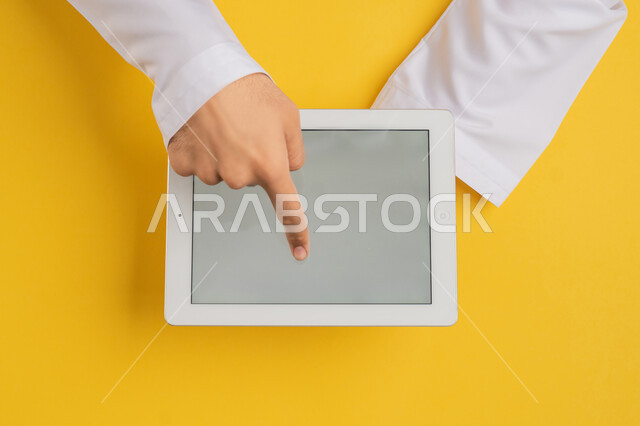 عرض شاشة رمادية فارغة، انجاز المهام عن بعد، متابعة الدروس التعليمية، بورتريه علوي عامودي ليد رجل عربي خليجي اماراتي يقوم بالنقر باصبعه السبابة على شاشة جهاز التابلت، شاب سعودي يحمل بيده الآيباد، تصفح مواقع التواصل الاجتماعي، خلفية صفراء