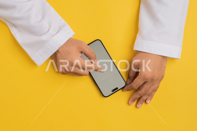 Browsing social media, displaying a blank gray screen, the development of technology and modern devices, a vertical portrait of an Arab Gulf Emirati man's hand tapping on a mobile phone screen, a Saudi young man using a mobile phone, yellow background