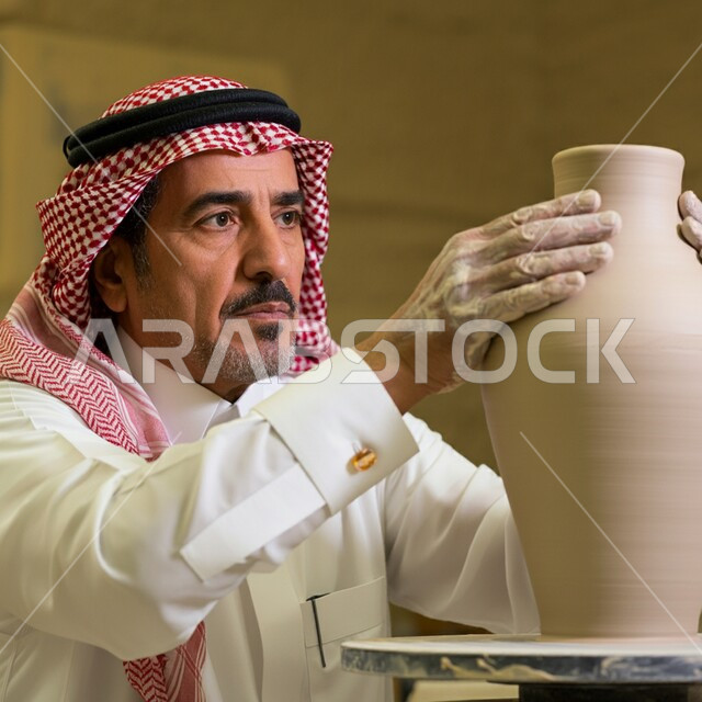 أعمال محلية وطنية بأيدي سعودية، احتراف العمل في صناعة الخزفيات، حرف وصناعات يدوية شعبية من التراث السعودي العريق، صنع الجرار الفخارية المزخرفة، أواني خزفية مصنوعة من الطين، رجل عربي خليجي سعودي يرتدي الثوب التقليدي يقوم بصنع إناء من الفخار