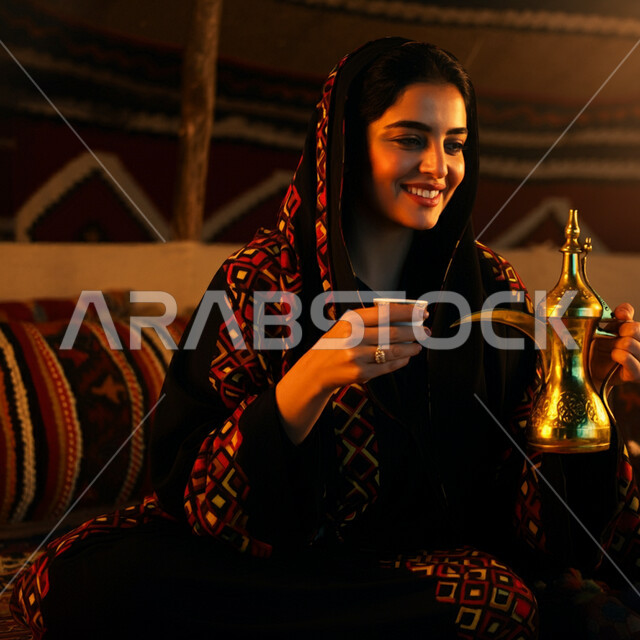  أصالة عادات وتقاليد المجتمع السعودي في المناسبات الاسلامية, كرم الضيافة وحسن الاستقبال في السعودية, صورة مقربة لشابة عربية خليجية سعودية مبتسمة ترتدي العباءة والحجاب تقوم بصب القهوة الخليجية, تقديم المشروبات الساخنة العربية الأصيلة في الأعياد