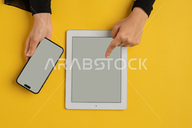 دمج التكنولوجيا الحديثة في الحياة اليومية والعملية، عرض شاشة رمادية فارغة، التسويق الالكتروني للتطبيقات، بورتريه علوي عامودي لايدي امرأة عربية خليجية سعودية تقوم بالنقرعلى جهاز التابلت، شابة اماراتية تستخدام الهاتف المحمول، خلفية صفراء