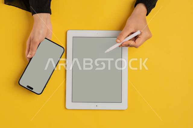 عرض شاشة رمادية فارغة، التسويق الالكتروني للتطبيقات، دمج التكنولوجيا الحديثة في الحياة اليومية والعملية، بورتريه علوي عامودي لايدي امرأة عربية خليجية سعودية تحمل الهاتف المحمول، شابة اماراتية تقوم باستخدام جهاز التابلت، خلفية صفراء