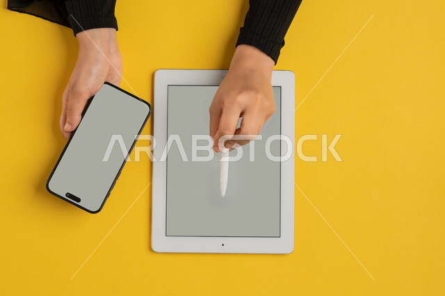 التسويق الالكتروني للتطبيقات، عرض شاشة رمادية فارغة، دمج التكنولوجيا الحديثة في الحياة اليومية والعملية، بورتريه علوي عامودي لايدي امرأة عربية خليجية سعودية تحمل الهاتف المحمول، شابة اماراتية تقوم باستخدام جهاز التابلت، خلفية صفراء