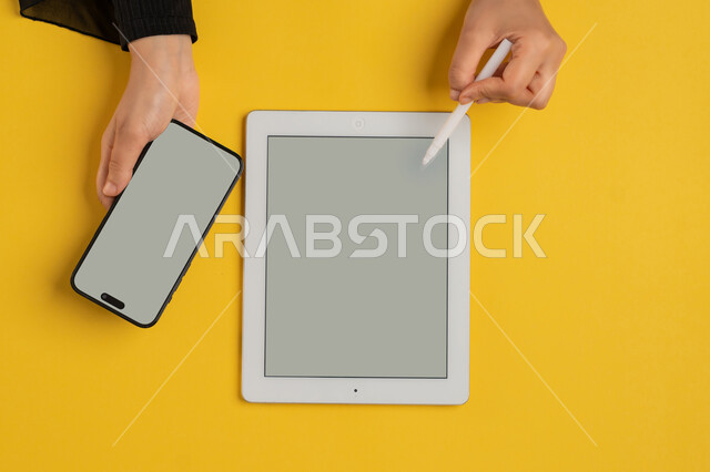 التسويق الالكتروني للتطبيقات، عرض شاشة رمادية فارغة، دمج التكنولوجيا الحديثة في الحياة اليومية والعملية، بورتريه علوي عامودي لايدي امرأة عربية خليجية سعودية تحمل الهاتف المحمول، شابة اماراتية تقوم باستخدام جهاز التابلت، خلفية صفراء