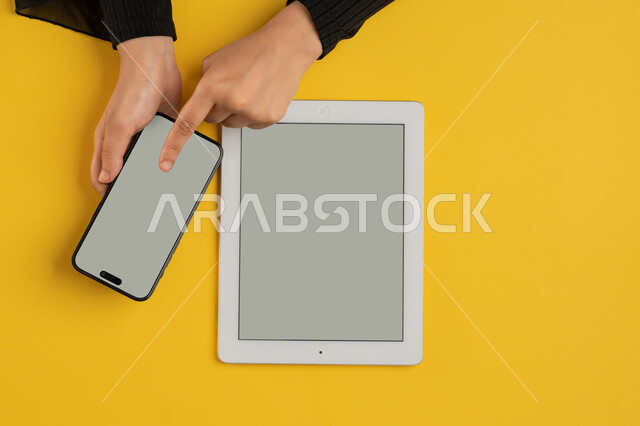 عرض شاشة رمادية فارغة، التسويق الالكتروني للتطبيقات، دمج التكنولوجيا الحديثة في الحياة اليومية والعملية، بورتريه علوي عامودي لايدي امرأة عربية خليجية سعودية تقوم بالنقرعلى الهاتف المحمول، شابة اماراتية تستخدام جهاز التابلت، خلفية صفراء
