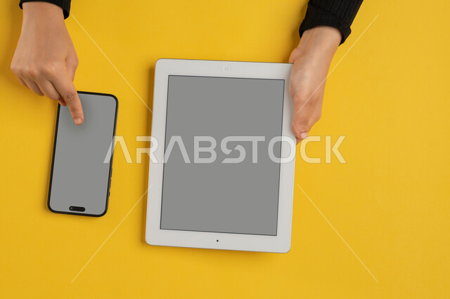 عرض شاشة رمادية فارغة، التسويق الالكتروني للتطبيقات، دمج التكنولوجيا الحديثة في الحياة اليومية والعملية، بورتريه علوي عامودي لايدي امرأة عربية خليجية سعودية تقوم بالنقرعلى الهاتف المحمول، شابة اماراتية تستخدام جهاز التابلت، خلفية صفراء