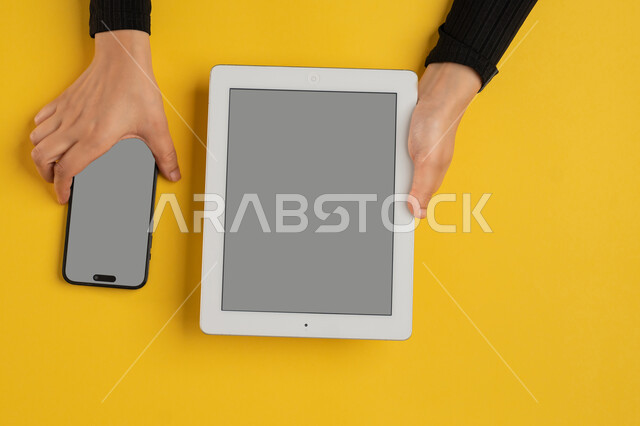 Blank gray screen, e-marketing for applications, integration of modern technology into daily and business life, vertical overhead portrait of a Saudi Arabian Gulf woman holding a mobile phone, young Emirati woman using a tablet, yellow background