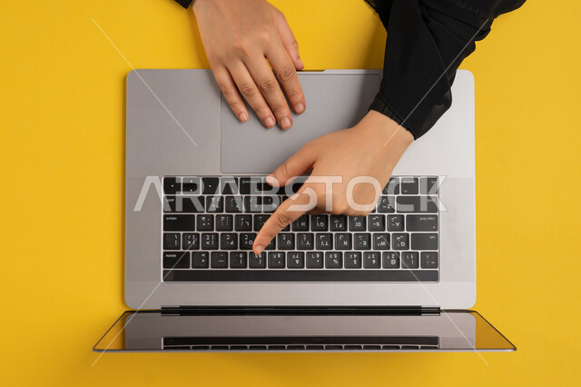 دمج التكنولوجيا الحديثة في الحياة العملية، إنجاز المهام المطلوبة عن بعد، بورتريه علوي عامودي لايدي امرأة عربية خليجية اماراتية تعمل على الحاسب المحمول، شابة سعودية ترتدي العباءة تقوم بالكتابة على لوحة المفاتيح، مفهوم ادارة الاعمال وتحقيق الأهداف، خلفية صفراء
